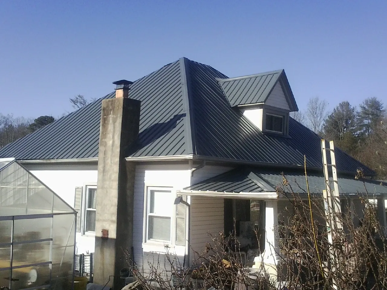 Dark blue standing seam metal roof on a white farmhouse with dormer — Slate & Tile Roof Repair by Roofing Brothers in Golden Valley
