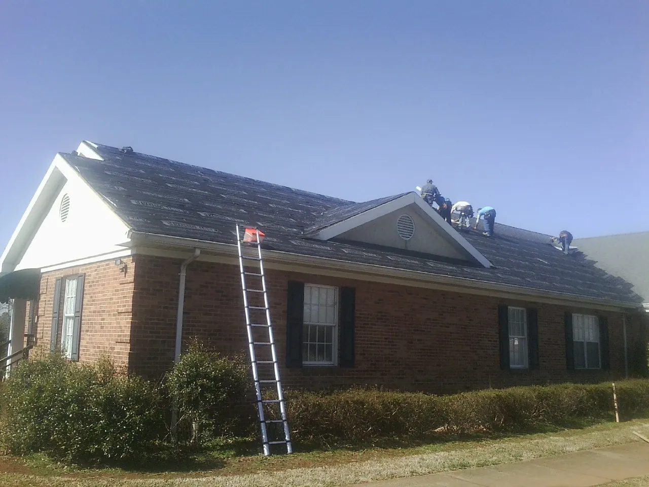 Crew tearing shingles off a brick ranch roof with a ladder set — Emergency Roof Repair work by our crew in Golden Valley