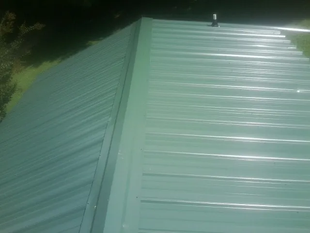 New green metal panels meeting at the ridge of a roof — Flat Roof Repair work by our crew in Golden Valley