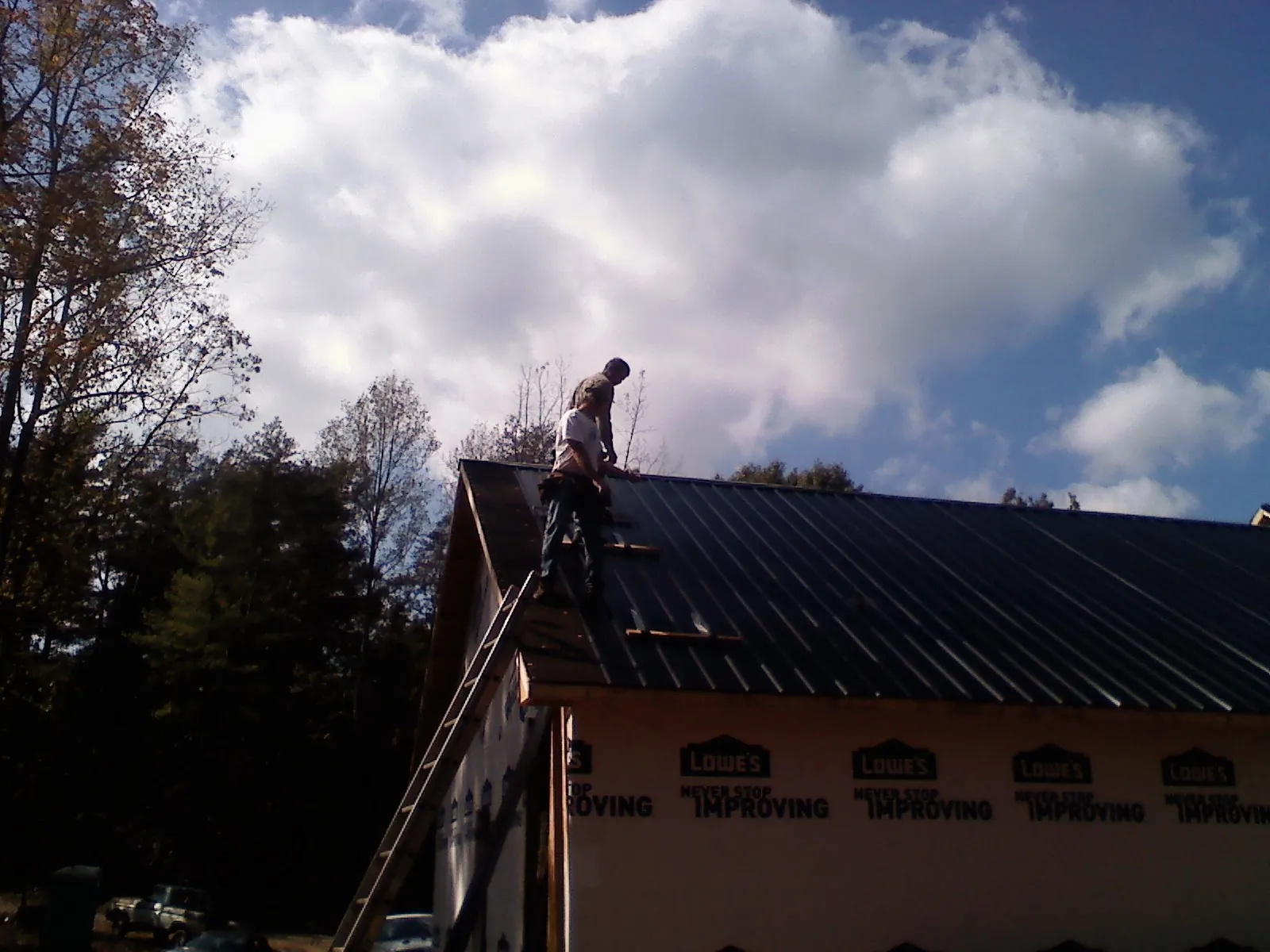 Roofer fastening dark metal panels high against a cloudy sky, from a Roof Inspection job in Golden Valley