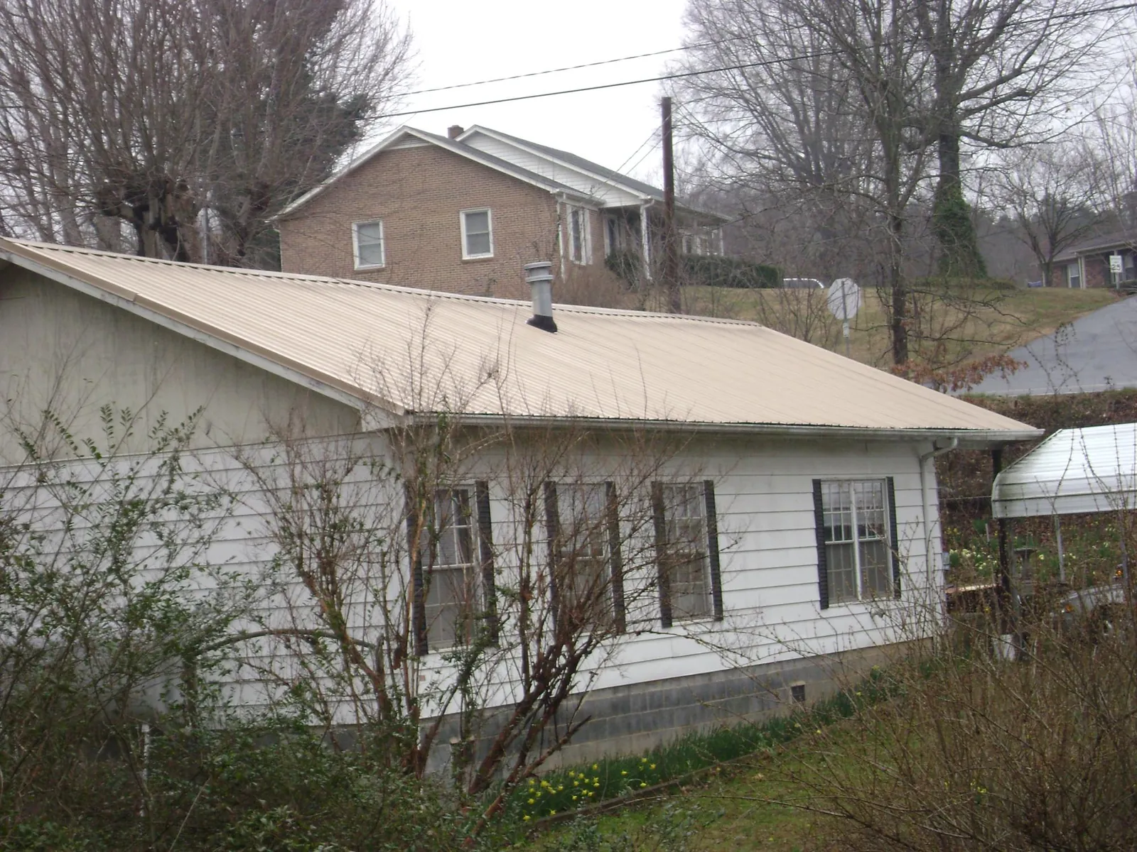 Tan metal roof on a white sided house set into a hillside — Commercial Roofing by Roofing Brothers in Golden Valley